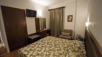 A hotel room with a bed, a desk, a chair, a television, and a window with curtains.