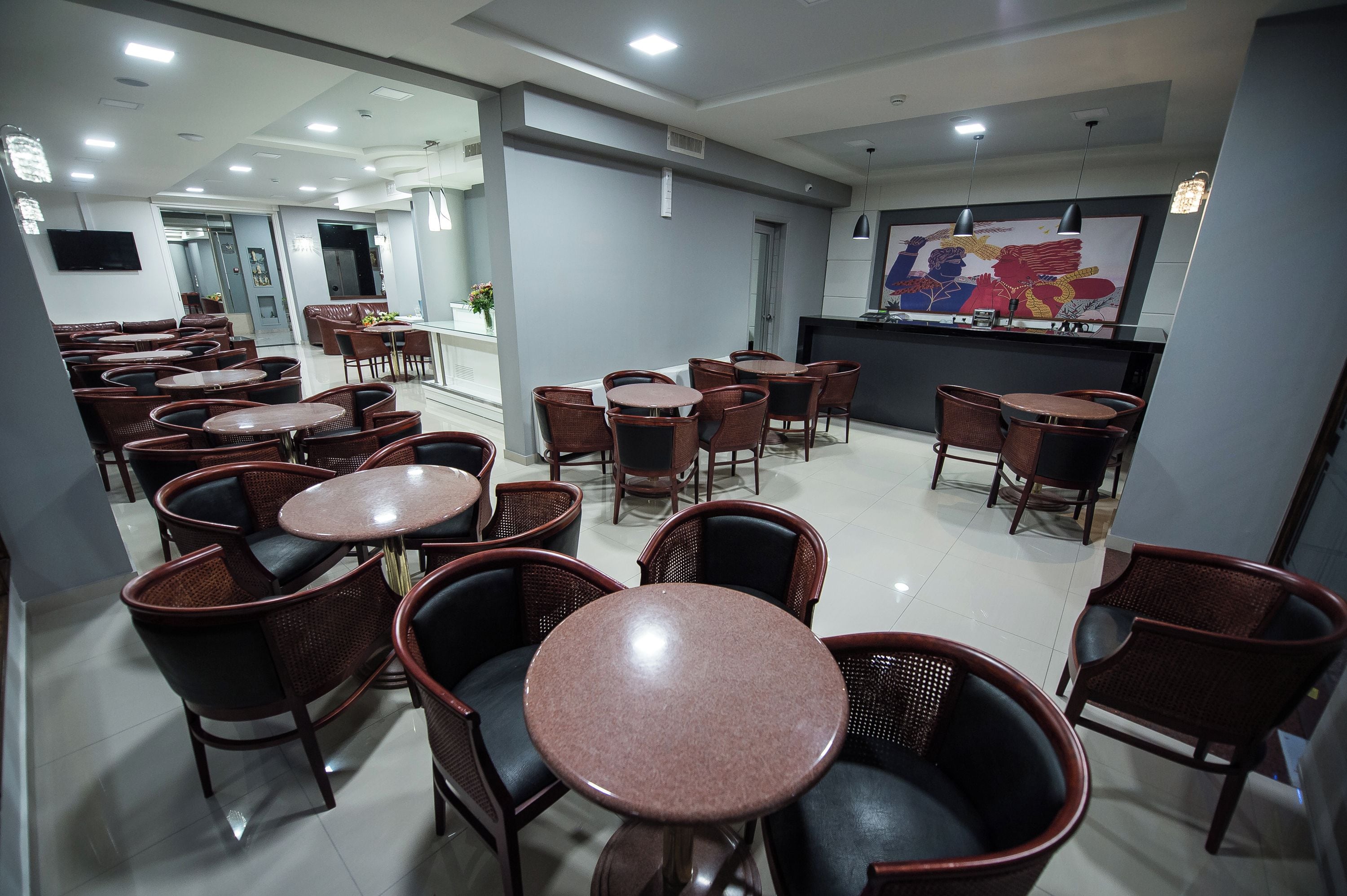 A restaurant with round tables and wicker chairs, a counter with a menu, and a large wall mural.
