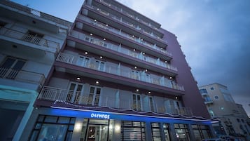 Een hotel met meerdere verdiepingen, balkons, een restaurant genaamd 'ONYMNOZ' op de begane grond en een parkeerplaats ervoor.