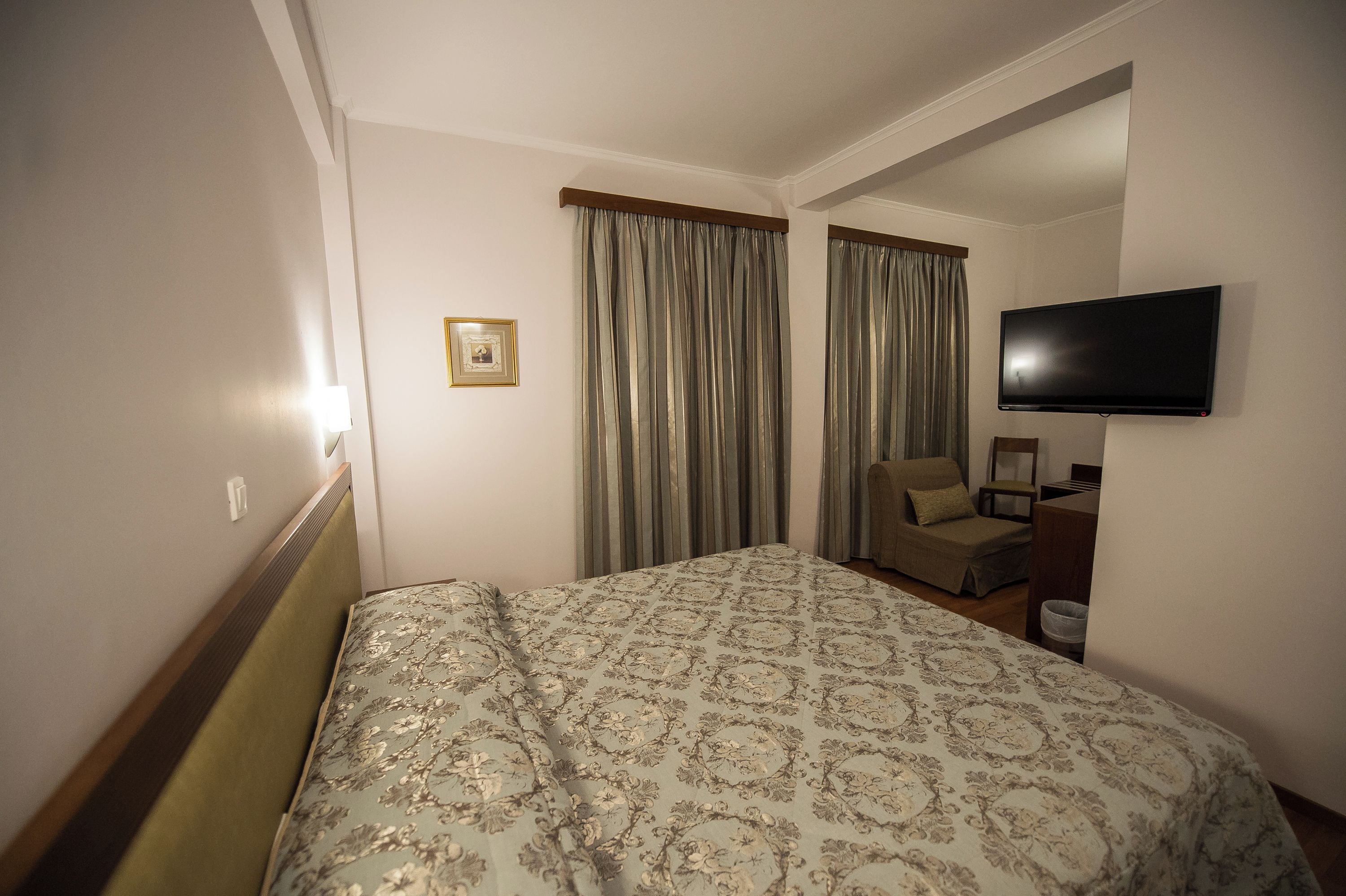 Ein Hotelzimmer mit einem Bett, einem Sessel, einem Fernseher und einem Bild an der Wand.