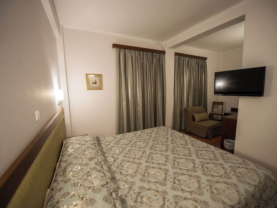 A hotel room with a bed, a chair, a television, and a picture on the wall.