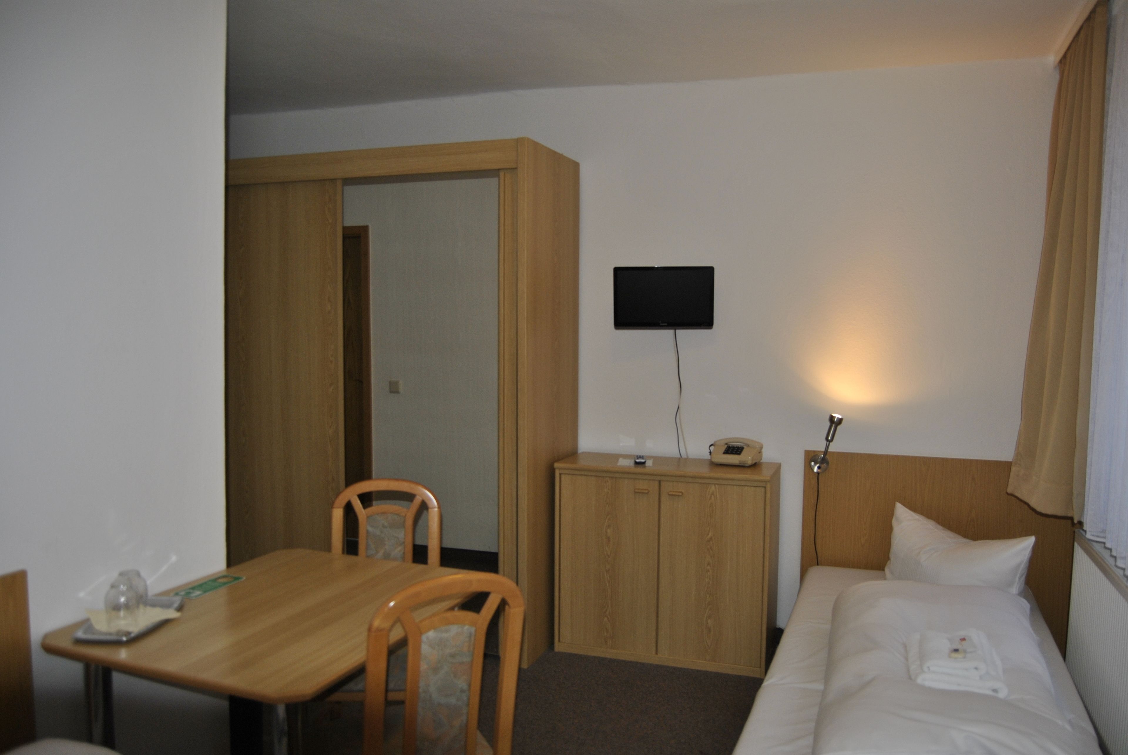 A hotel room with a bed, a desk, a chair, a television, and a wardrobe.