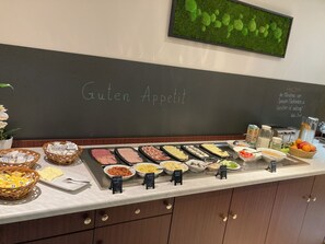 Mostrador de buffet con diferentes alimentos y un letrero de pizarra que dice 'Guten Appetit'.