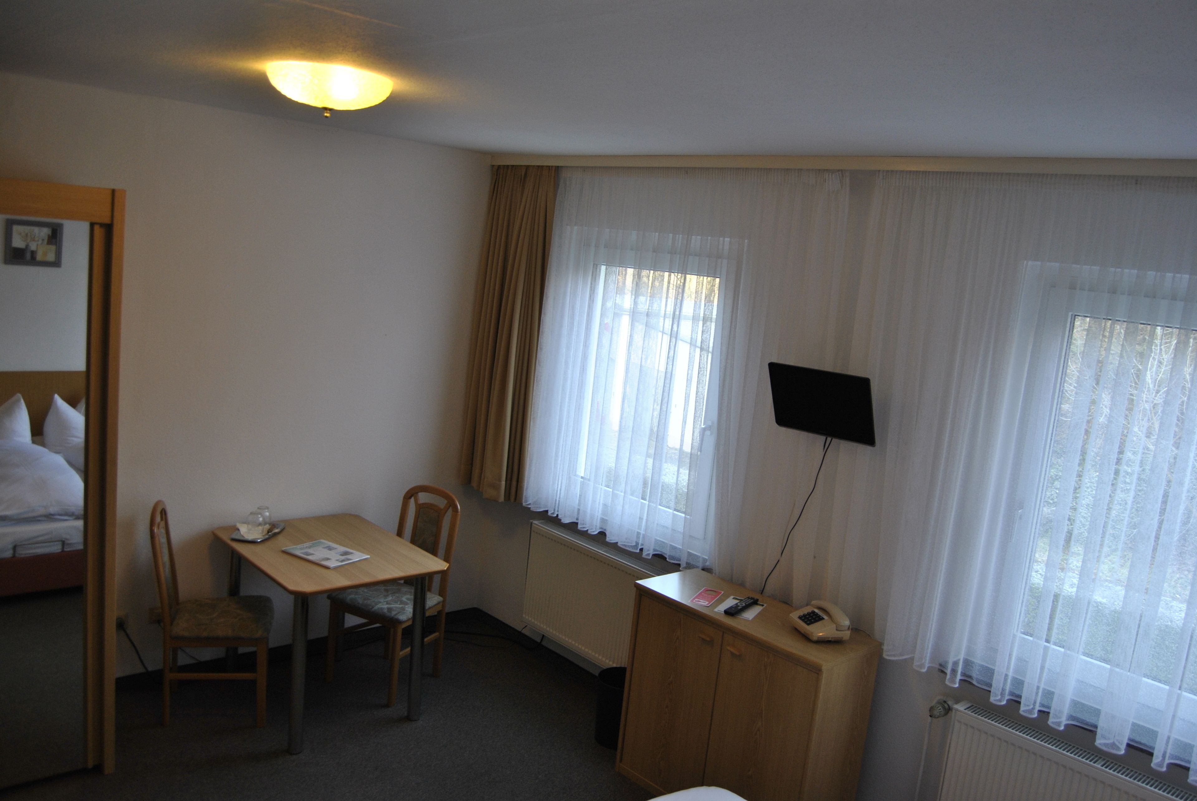A hotel room with a bed, a desk with a chair, a telephone, and a TV mounted on the wall.
