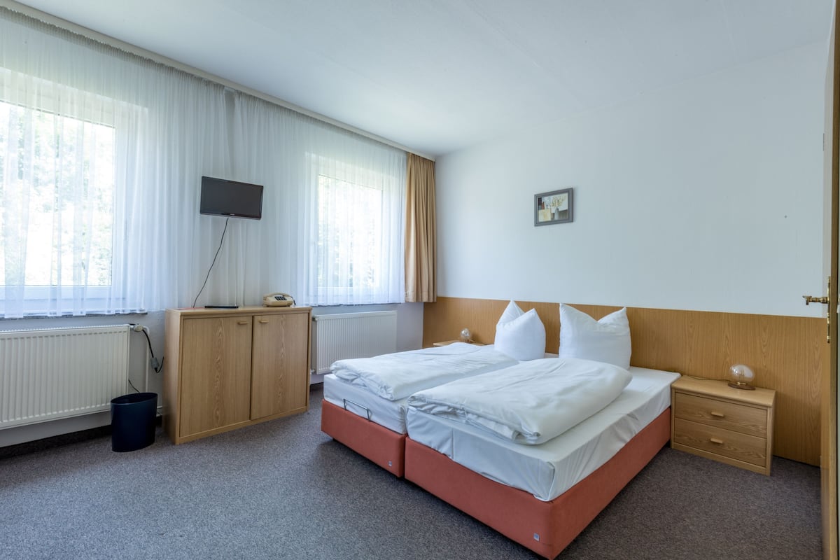 Une chambre d’hôtel avec un lit double, un téléviseur fixé au mur, une armoire en bois et une petite table de chevet.