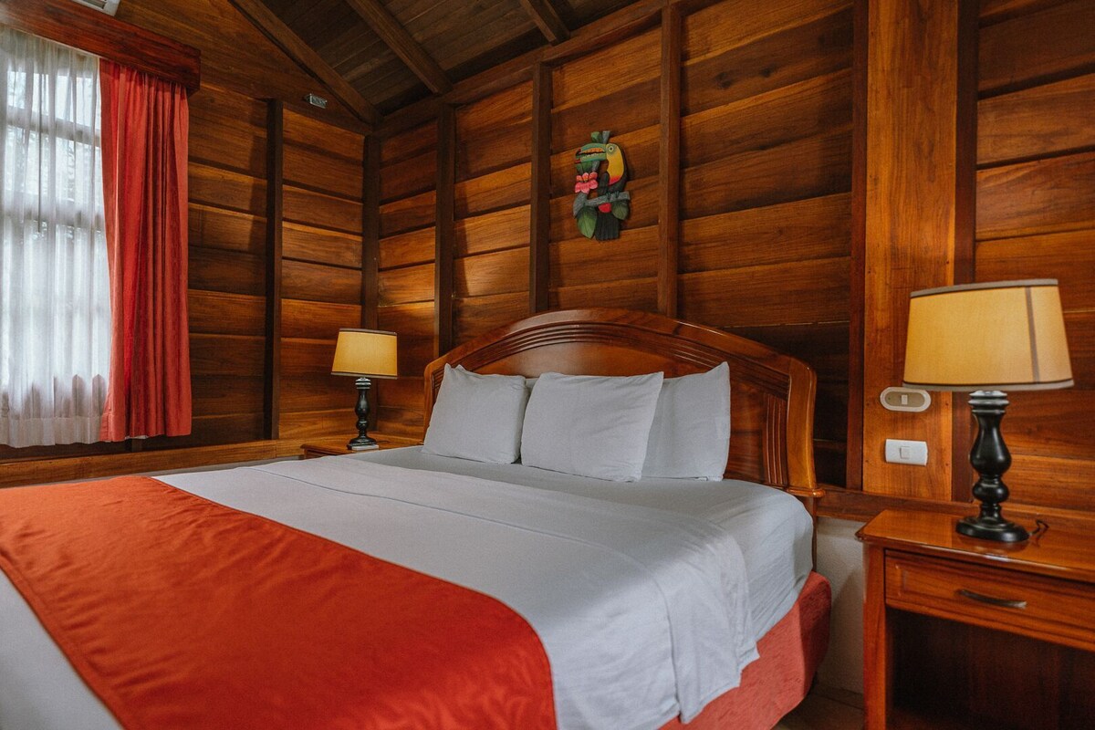 A wooden-paneled room with a bed, two bedside tables with lamps, and a window with curtains.