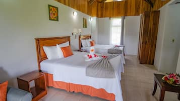 Una habitación de hotel con techo de madera, una cama grande con ropa de cama blanca y naranja, una mesita de noche pequeña y una mesita auxiliar.