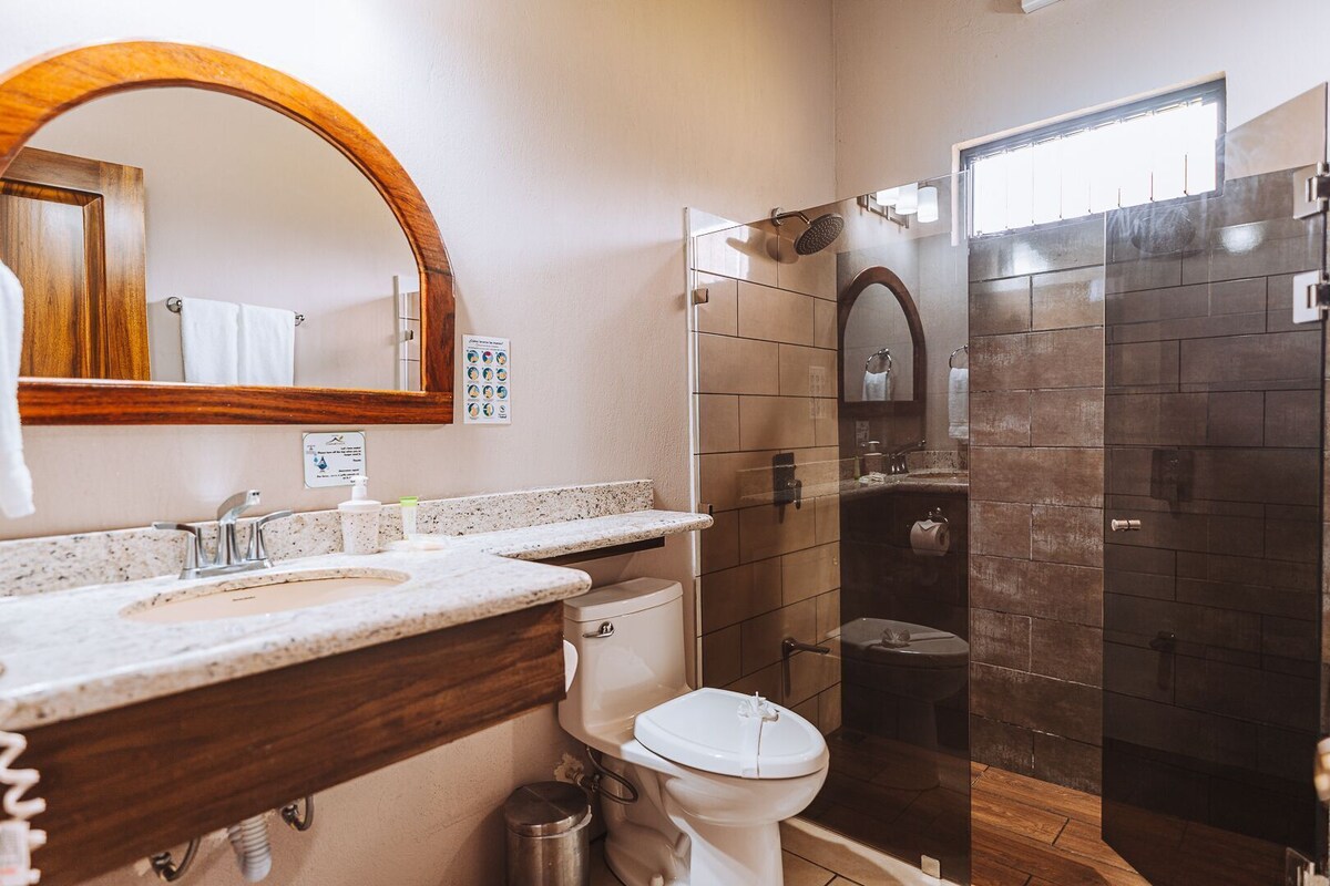A bathroom with a wooden vanity, a white toilet, a shower enclosure, and a mirror.