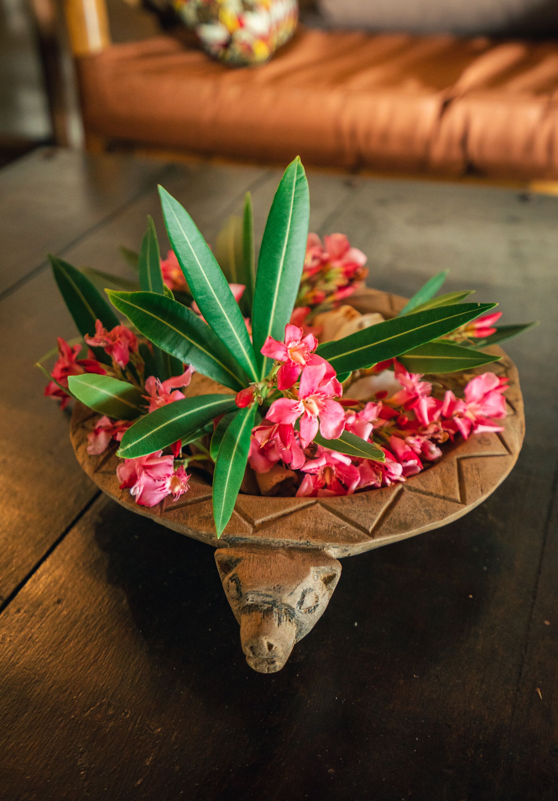 A wooden tray with green leaves and pink flowers on a dark wooden table.