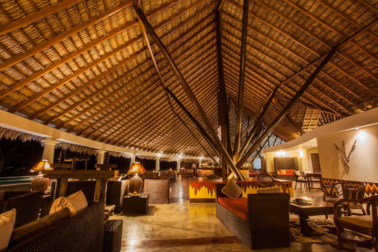 An indoor lounge area with a thatched roof, wicker furniture, and a bar area.