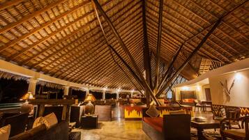 An indoor lounge area with a thatched roof, wicker furniture, and a bar area.
