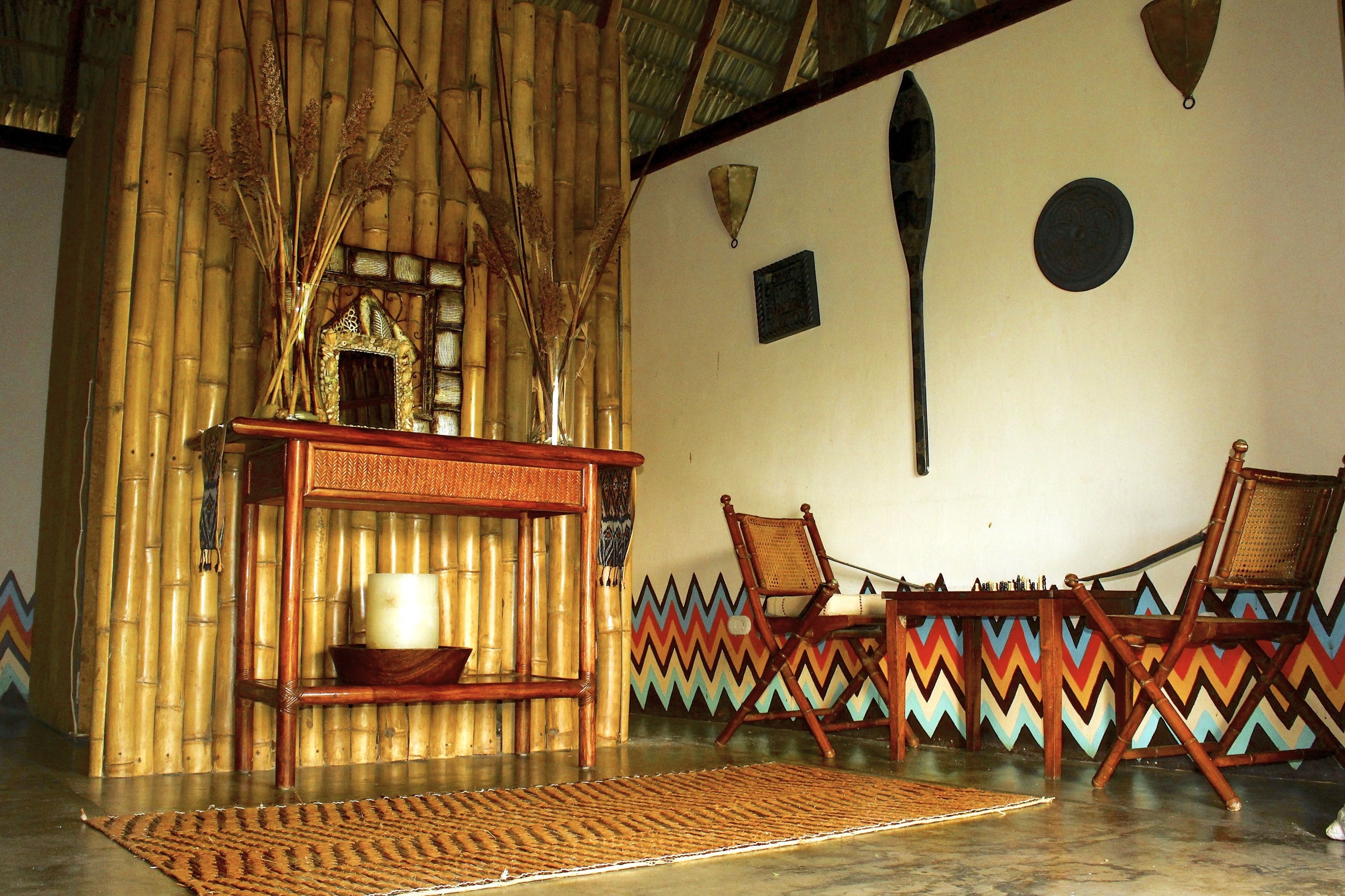 Une pièce aux murs recouverts de bambou, avec un tapis tressé et deux chaises en bois.