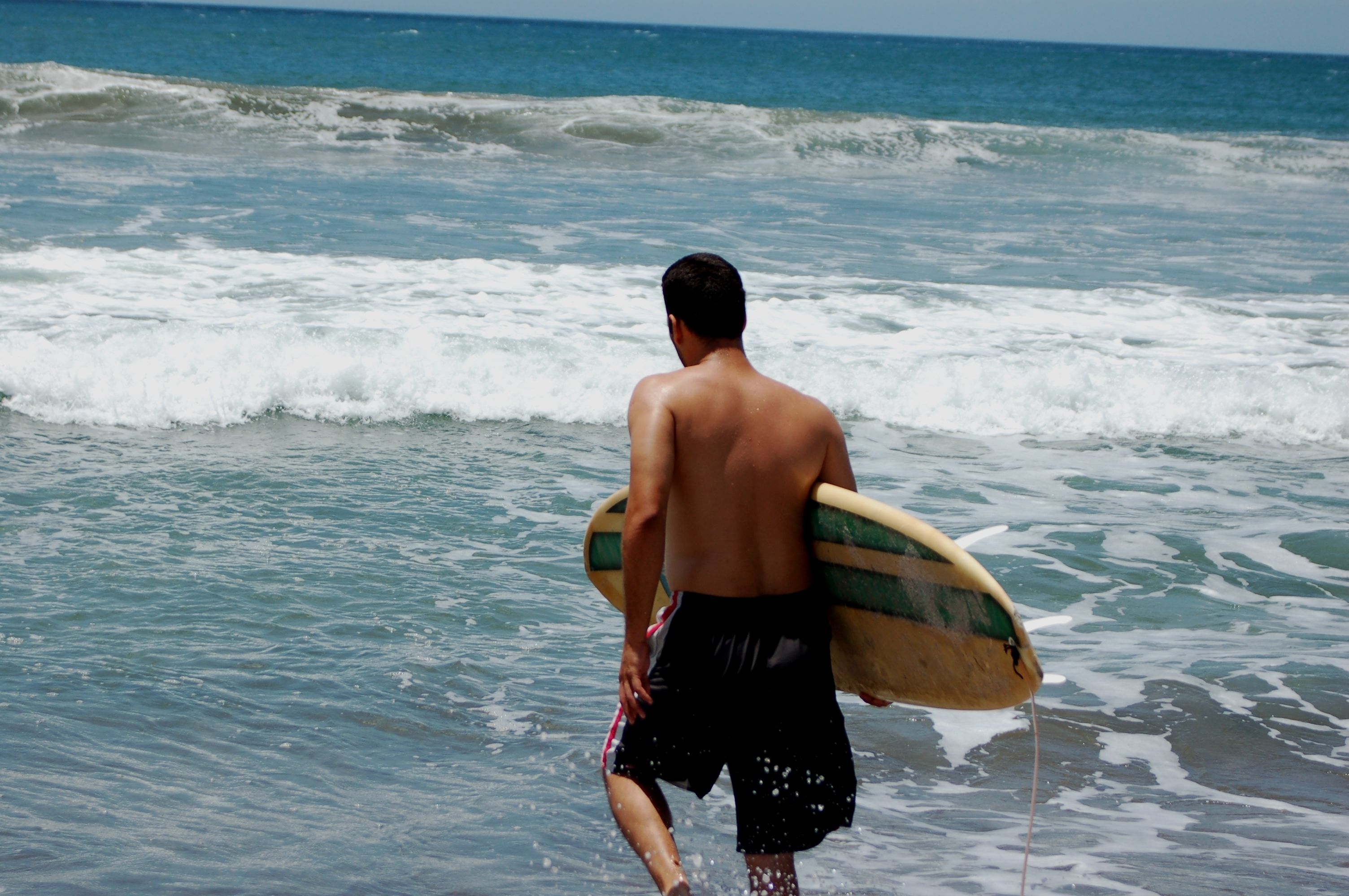 Una persona camina cap al mar portant una taula de surf.