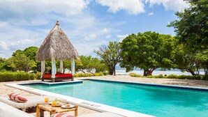 A pool area with lounge chairs, a thatched gazebo, and a view of the sea. - Hotel Punta Teonoste Boutique Beachfront Resort (Tola)