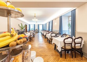 Un comedor con filas de mesas y sillas, una exhibición de frutas y una lámpara de cristal.