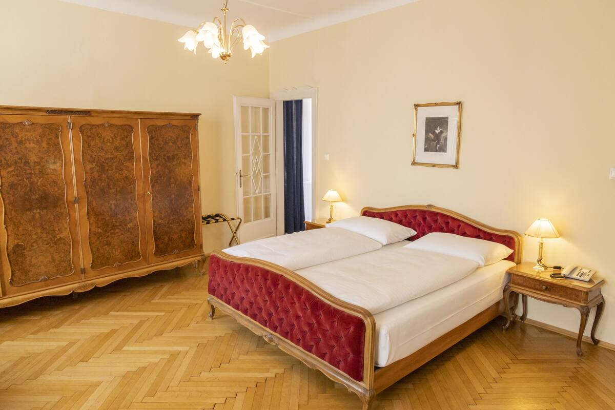 A bedroom with a large bed, wooden wardrobe, and a chandelier.