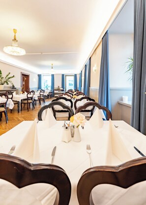 A dining area with tables set for a meal, featuring white tablecloths, dark wooden chairs, and a chandelier. - Hotel Mariahilf (Graz)