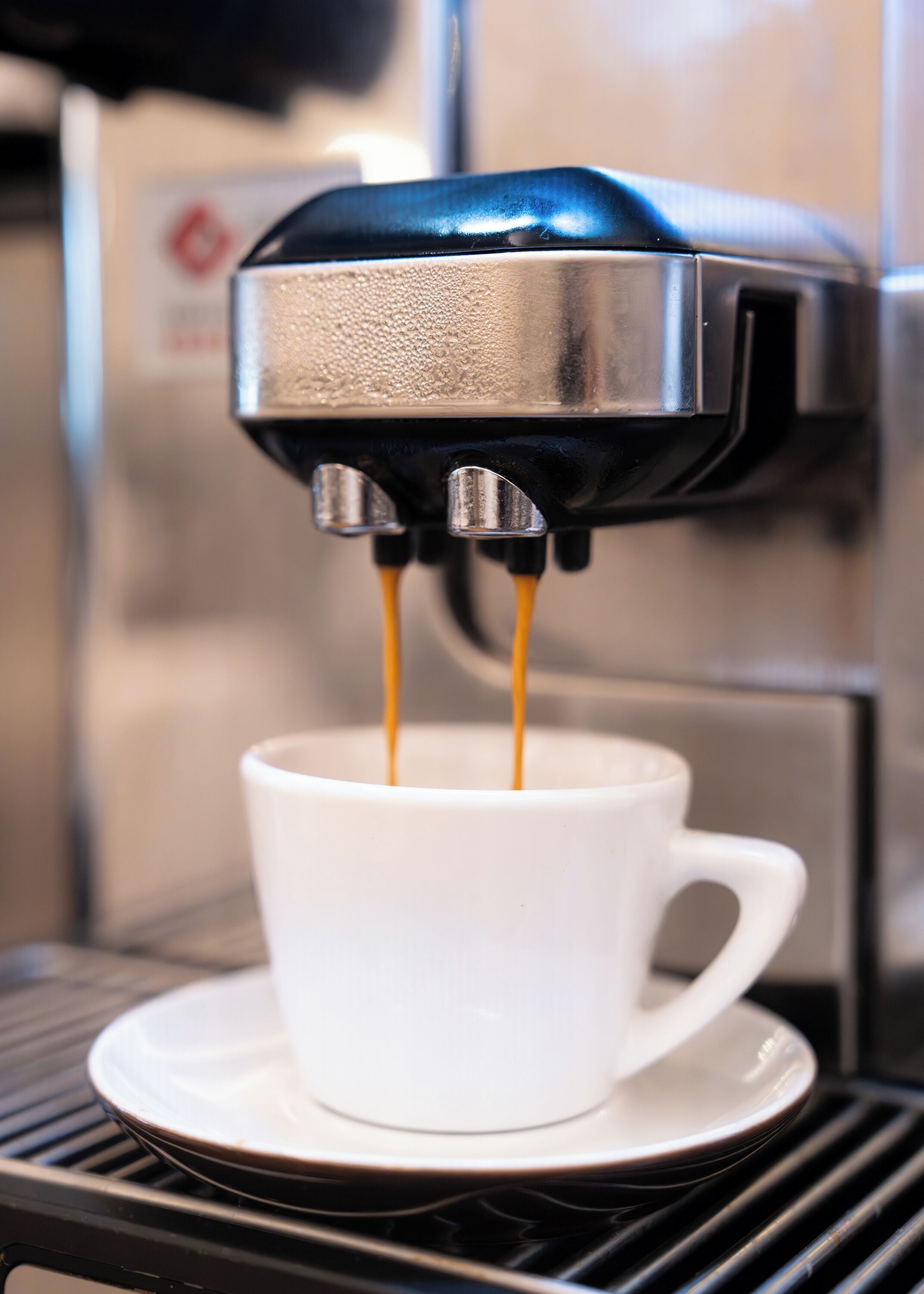 Una máquina de café sirviendo espresso en una taza blanca sobre una bandeja negra.