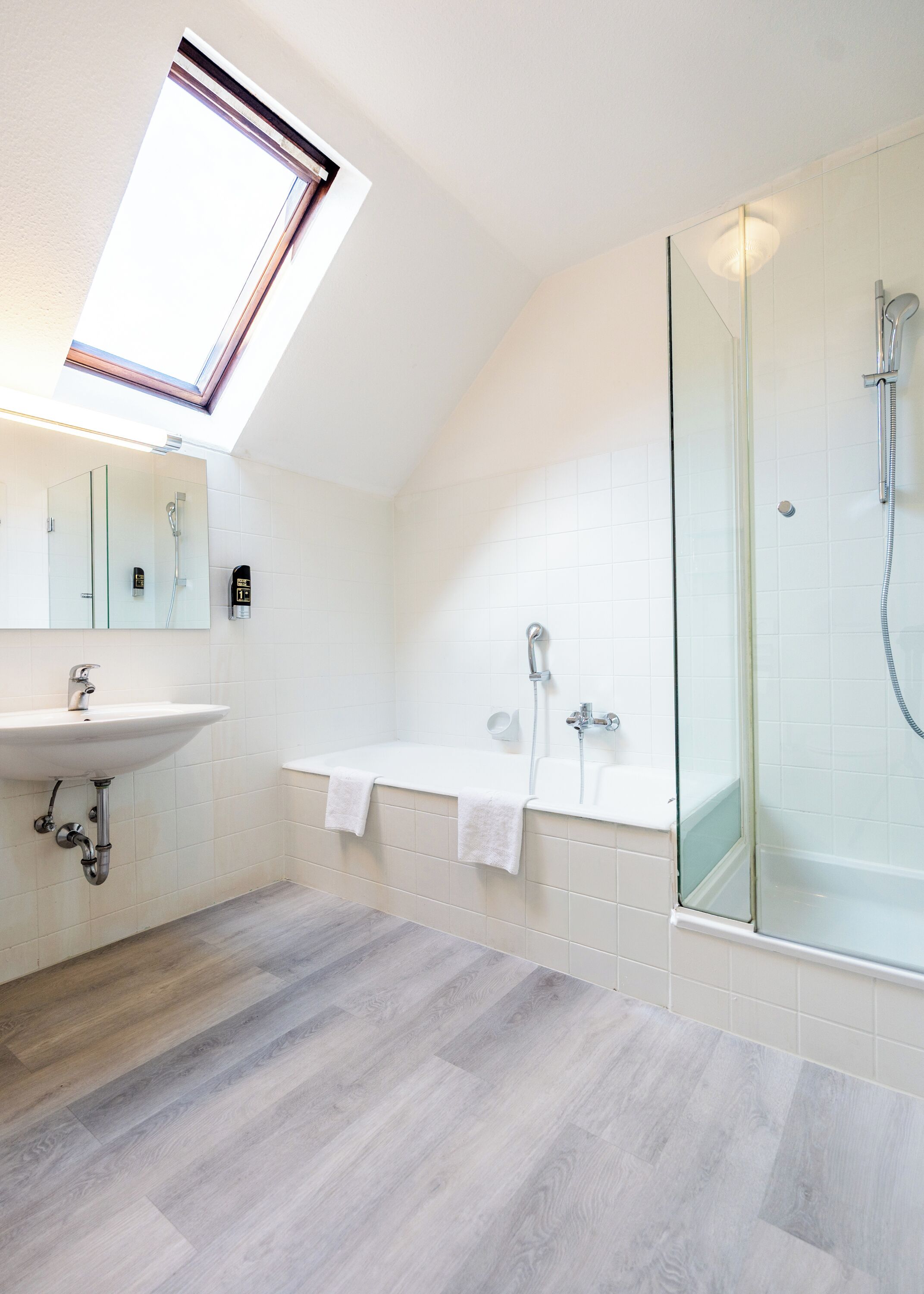A modern bathroom with a skylight, a freestanding bathtub, a glass-enclosed shower, and a sink with a mirror.