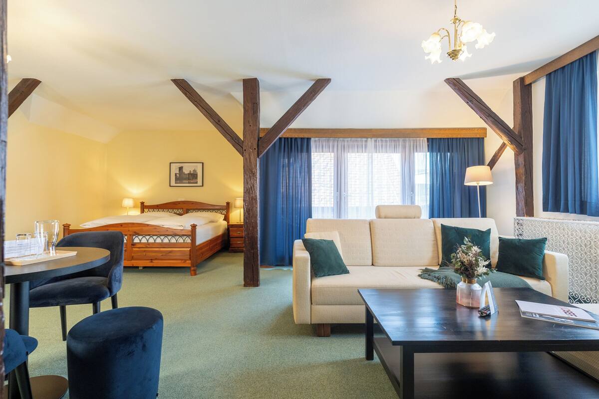 A hotel room with a bed, a sofa, a dining table, and a chandelier.