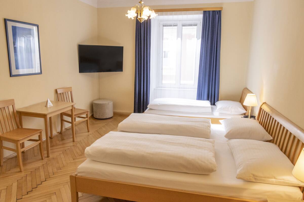 A hotel room with two beds, a desk, chairs, a TV, and a window with curtains.
