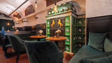 A restaurant interior with green upholstered seating, a decorative wall with a horse motif, and hanging light fixtures.