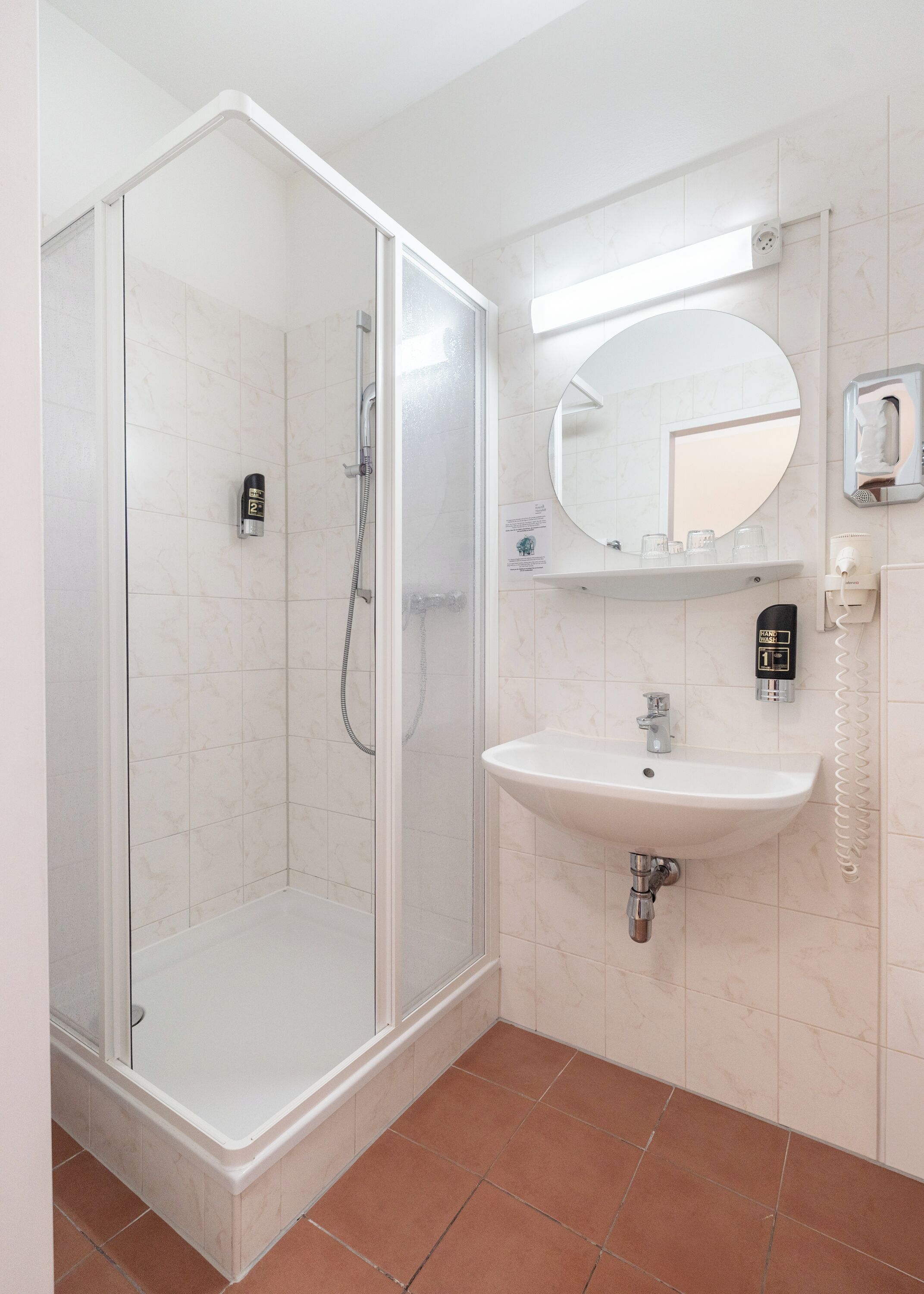 Une salle de bain moderne avec une douche à parois de verre, un lavabo avec un miroir au-dessus et une douchette à main.