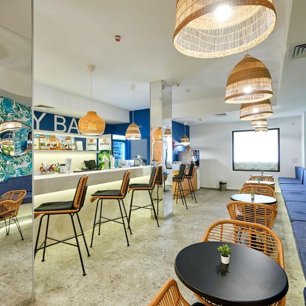 A modern bar area with wicker chairs, a counter with bar equipment, and a large screen. - Casablanca (Nessebar)