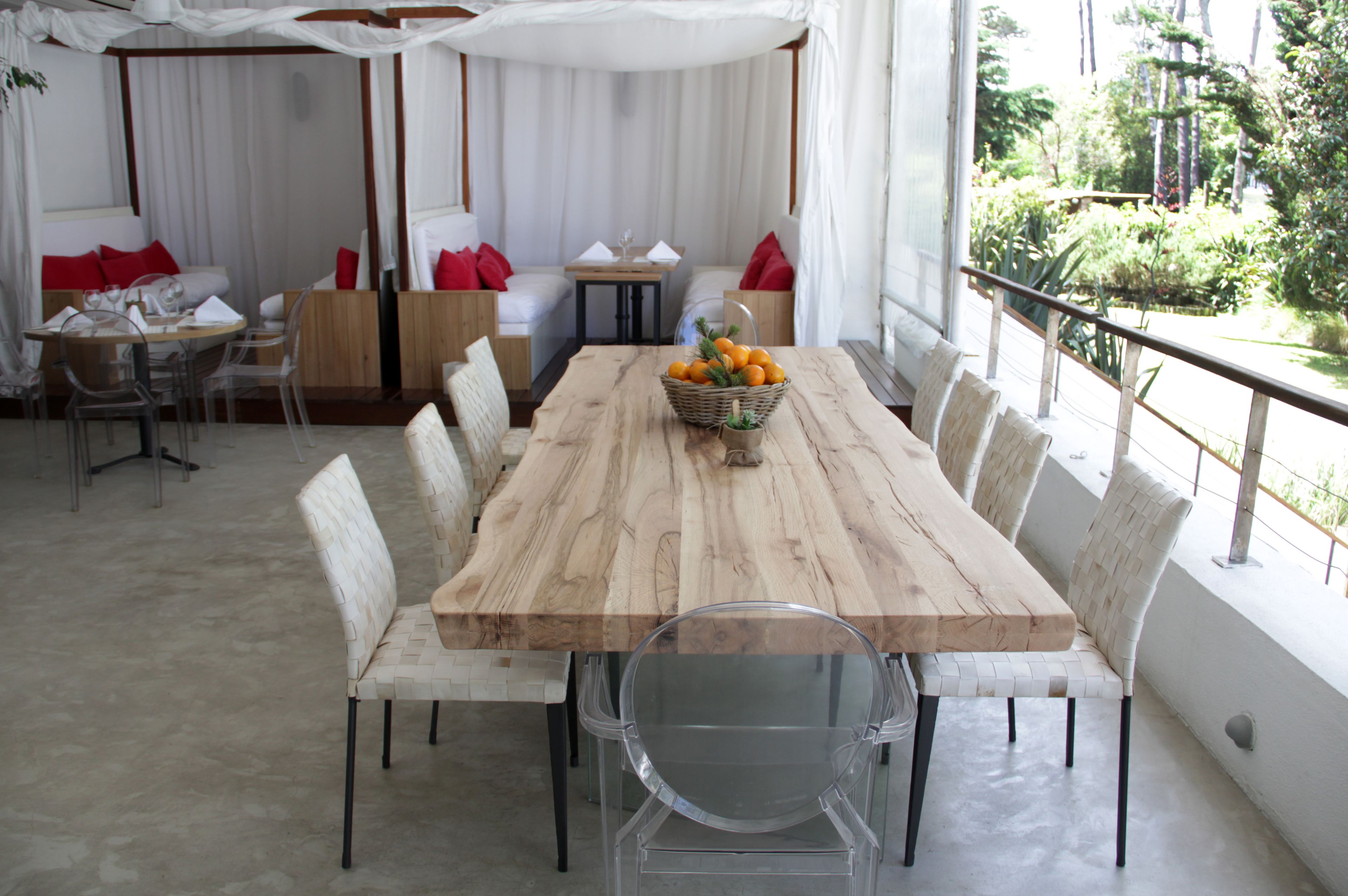 A wooden dining table with chairs, a basket of oranges, and a view of greenery outside.