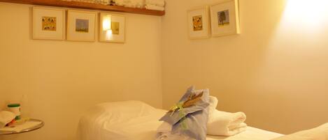 A hotel room with a bed, a shelf with toiletries, and framed pictures on the wall.