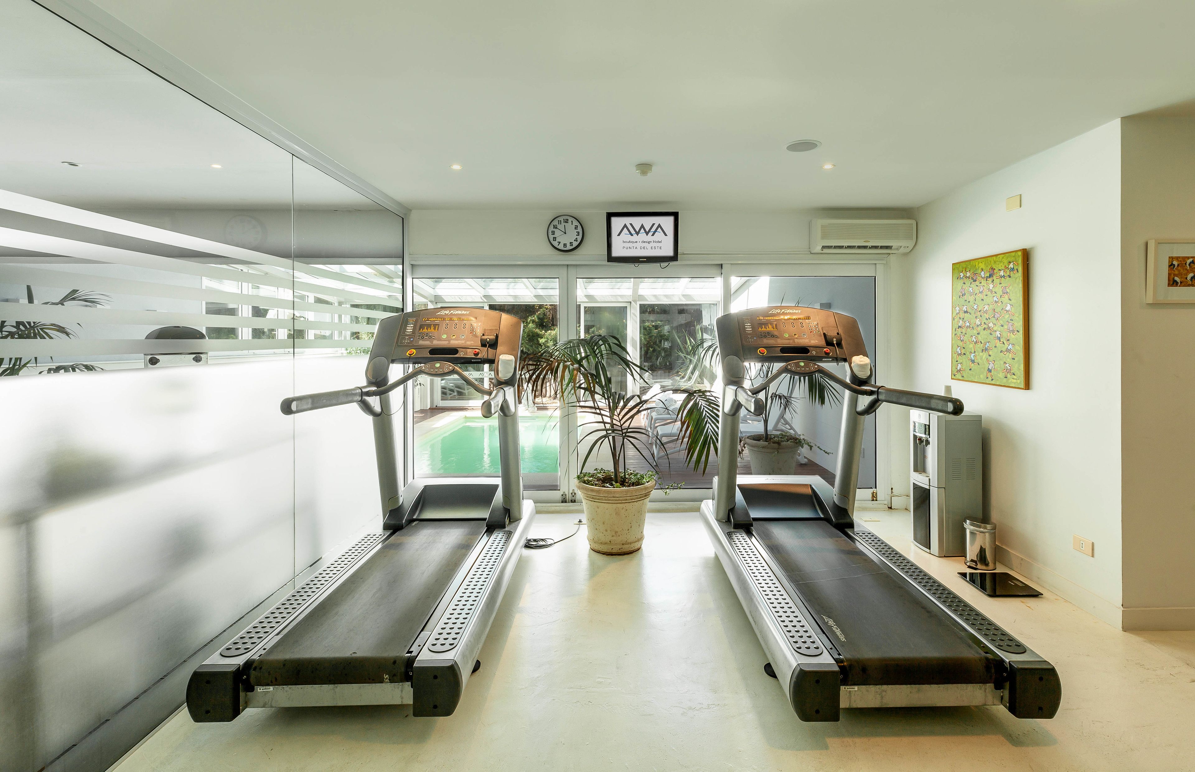 Un gimnasio con dos cintas de correr, una planta en maceta y un reloj en la pared.