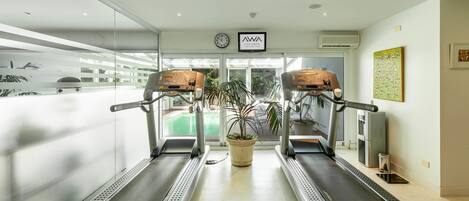 Un gimnasio con dos cintas de correr, una planta en maceta y un reloj en la pared.