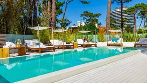 Une piscine entourée d’arbres et de bâtiments, avec des chaises longues et des parasols.