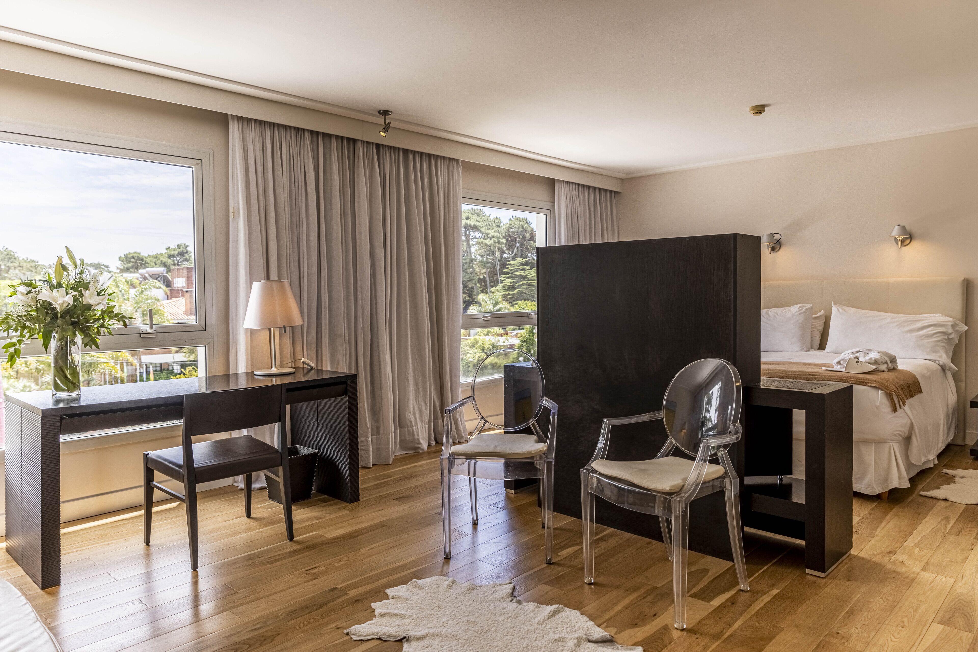 Une chambre d’hôtel moderne dotée d’un grand lit, d’un bureau, de deux chaises, d’un miroir et offrant une vue sur l’extérieur.