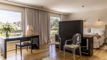 Habitación de hotel moderna con una cama grande, un escritorio, dos sillas, un espejo y vistas al exterior.