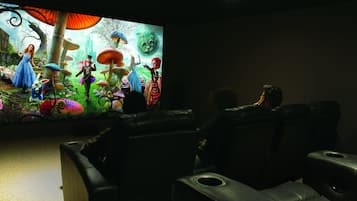 A dark room with a large screen displaying animated characters. There are leather sofas and a small table in the foreground.