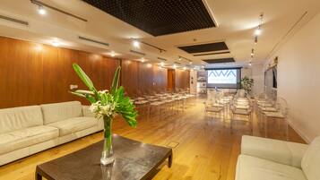 Une salle de conférence avec une longue table, des chaises transparentes, un canapé blanc et un écran de projection affichant le texte « AWA boutique + design Hotel Punta del Este ».