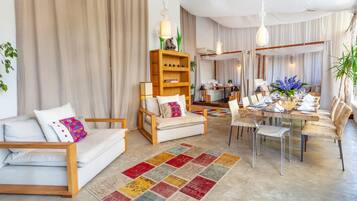 A modern living room with a sofa, dining table, chairs, and a bookshelf.