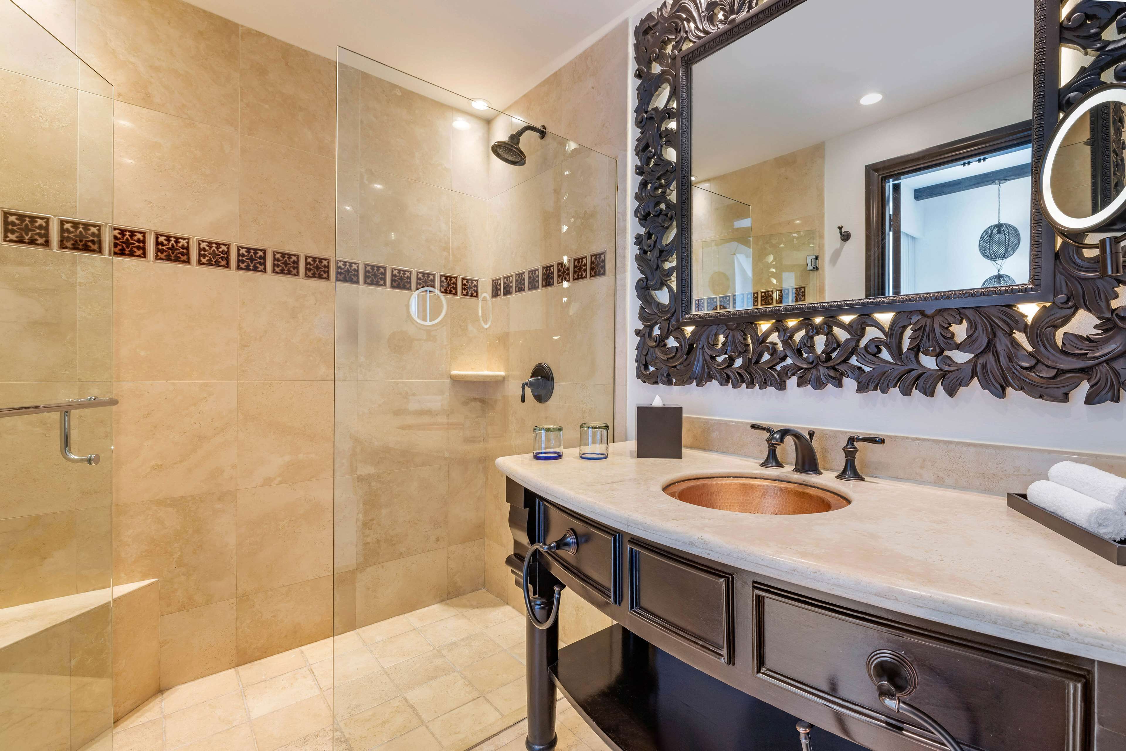 Une salle de bain moderne dotée d’une douche à parois de verre, d’un grand miroir décoratif et d’un lavabo avec un récipient en cuivre.