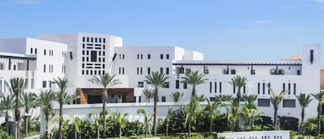 Un hotel moderno con architettura bianca, una piscina e palme.