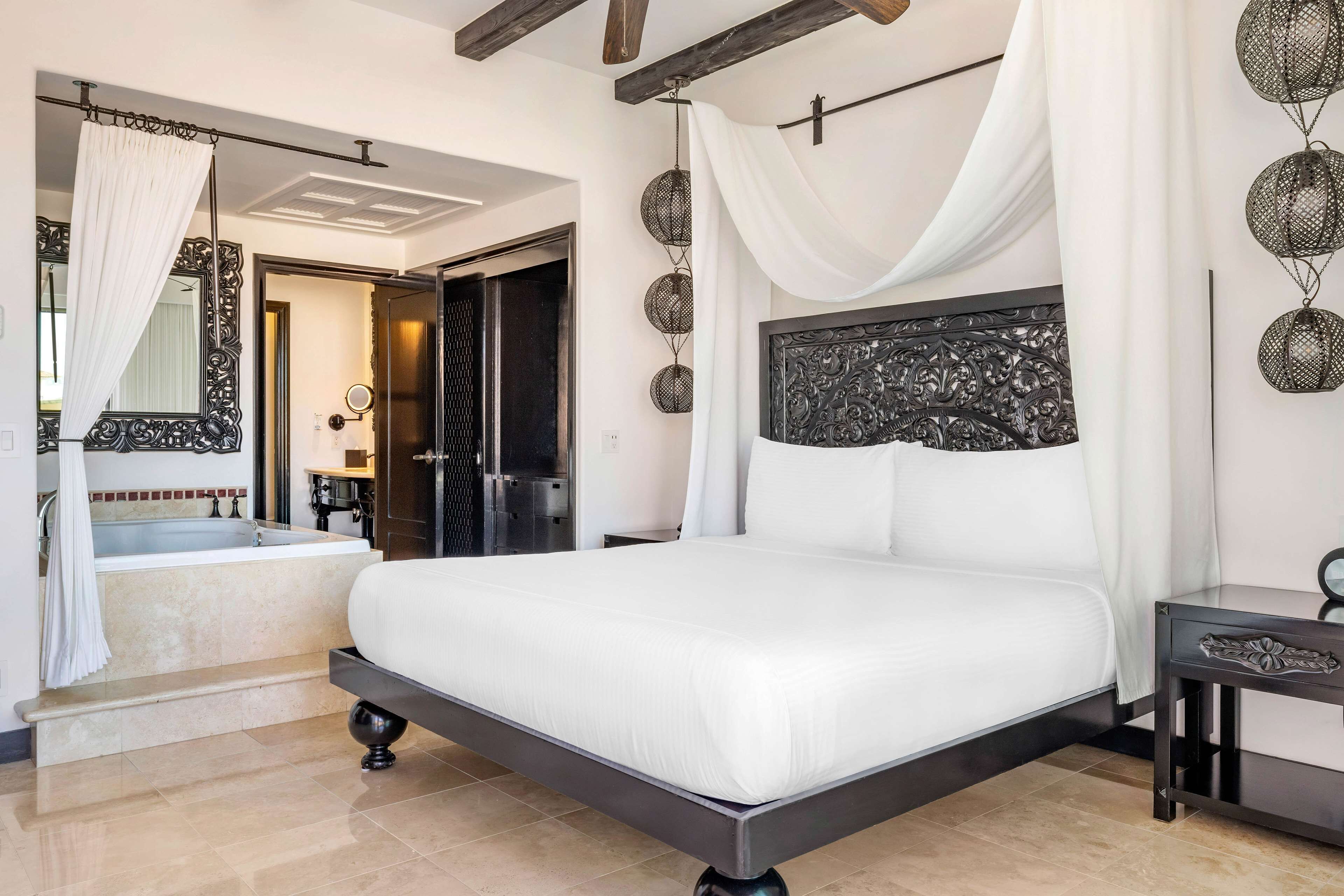 A modern bedroom with a large bed, a bathroom with a bathtub, and a dining area.