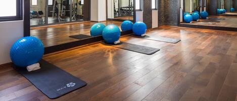 Un gimnasio con pelotas de ejercicio, piso de madera y espejos.