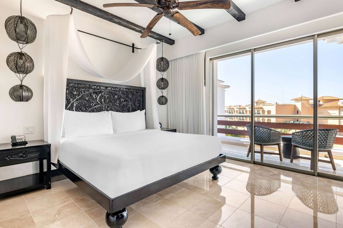 A modern hotel room with a large bed, a ceiling fan, and a balcony with outdoor furniture.