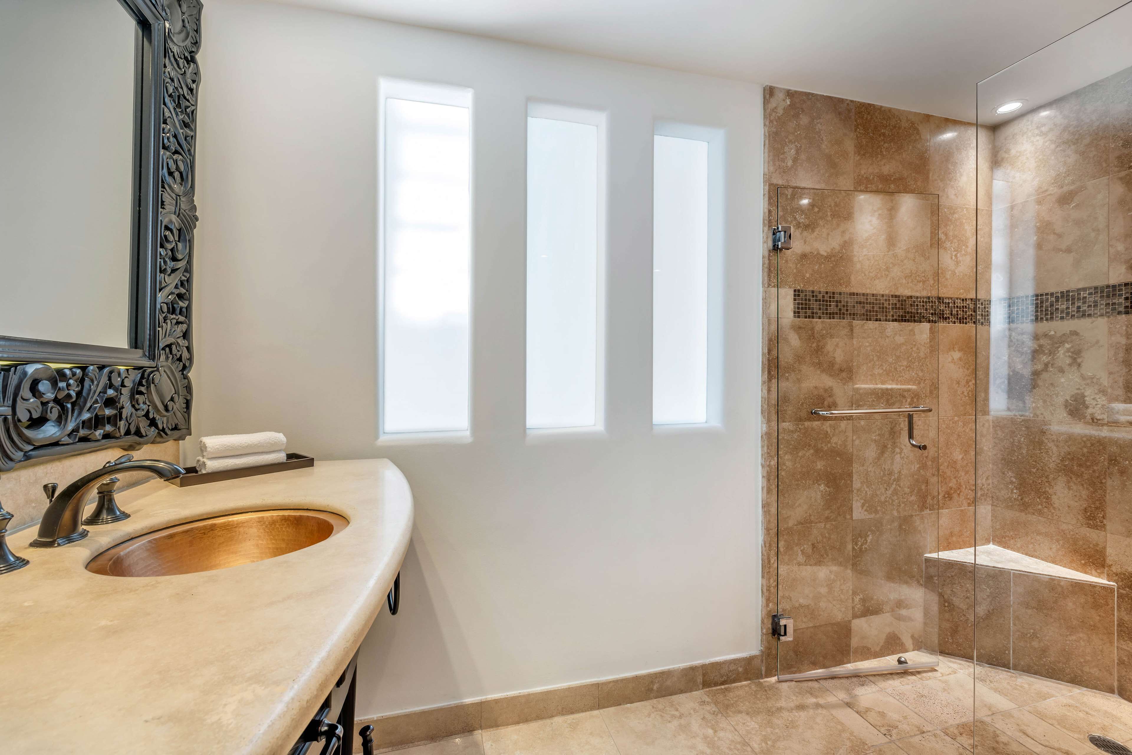 Un baño con un lavamanos grande, un espejo con un marco decorativo y una zona de ducha con mampara de vidrio.
