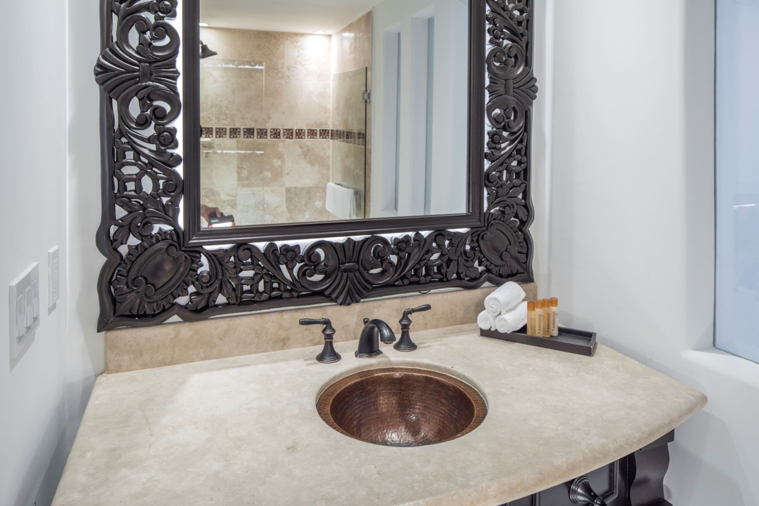 Un baño con un espejo grande y ornamentado, un lavabo de madera y un perchero.