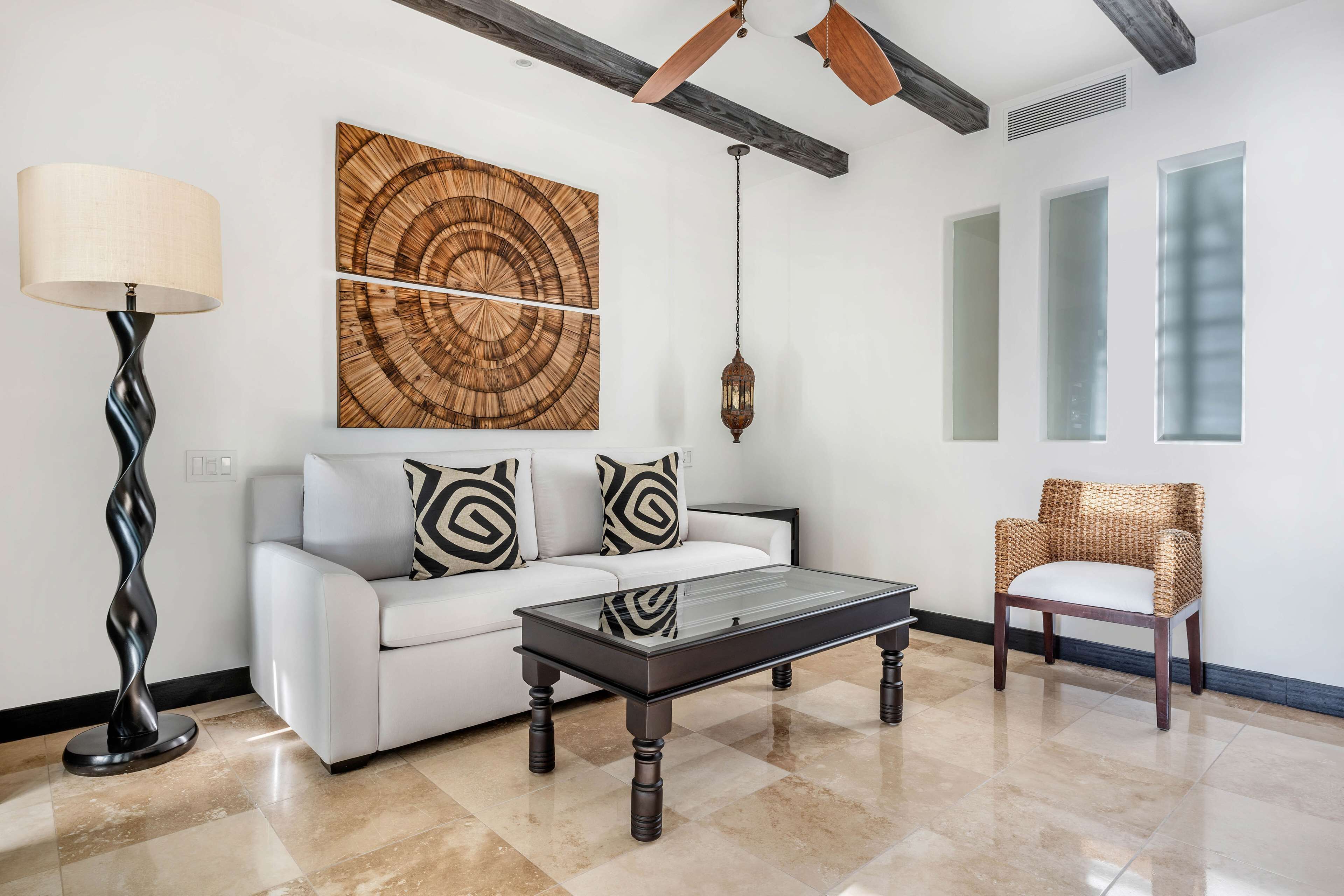 A modern living room with a glass coffee table, white sofa, and a wicker chair.