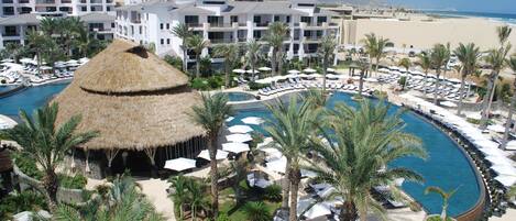 A resort with a central pool, multiple lounge areas, and a beach view.