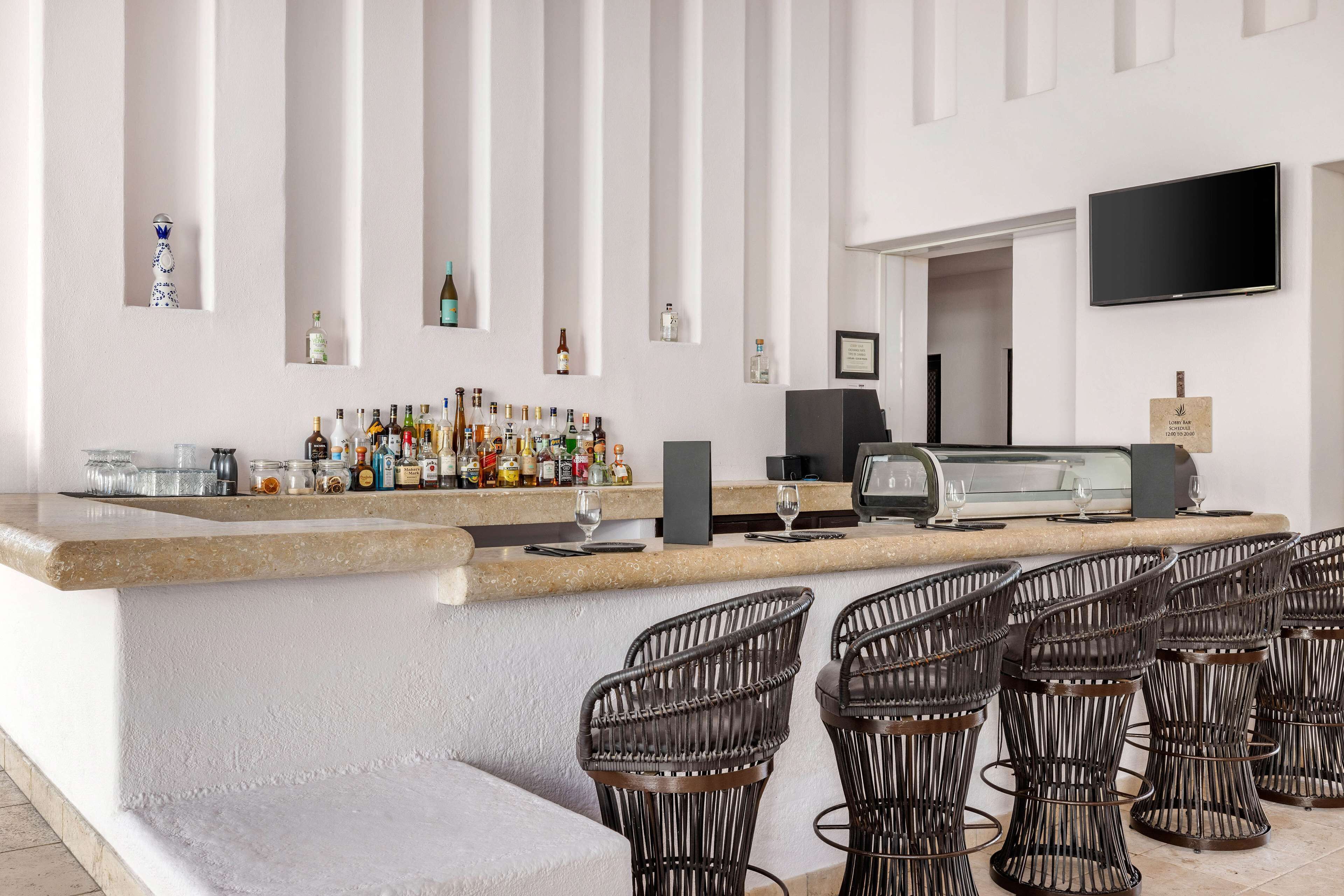 A bar area with a counter, bottles, glasses, and wicker chairs.