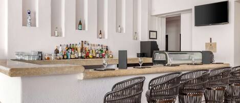 A bar area with a counter, bottles, glasses, and wicker chairs.