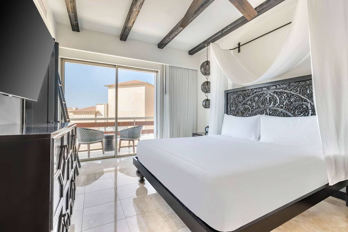 A bedroom with a large bed, a TV, and a balcony with a chair.